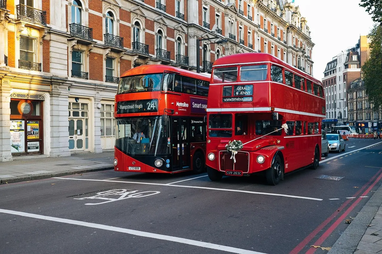 On the road across the capital — CS Services Red double-decker buses passing Victorian buildings on a London street
